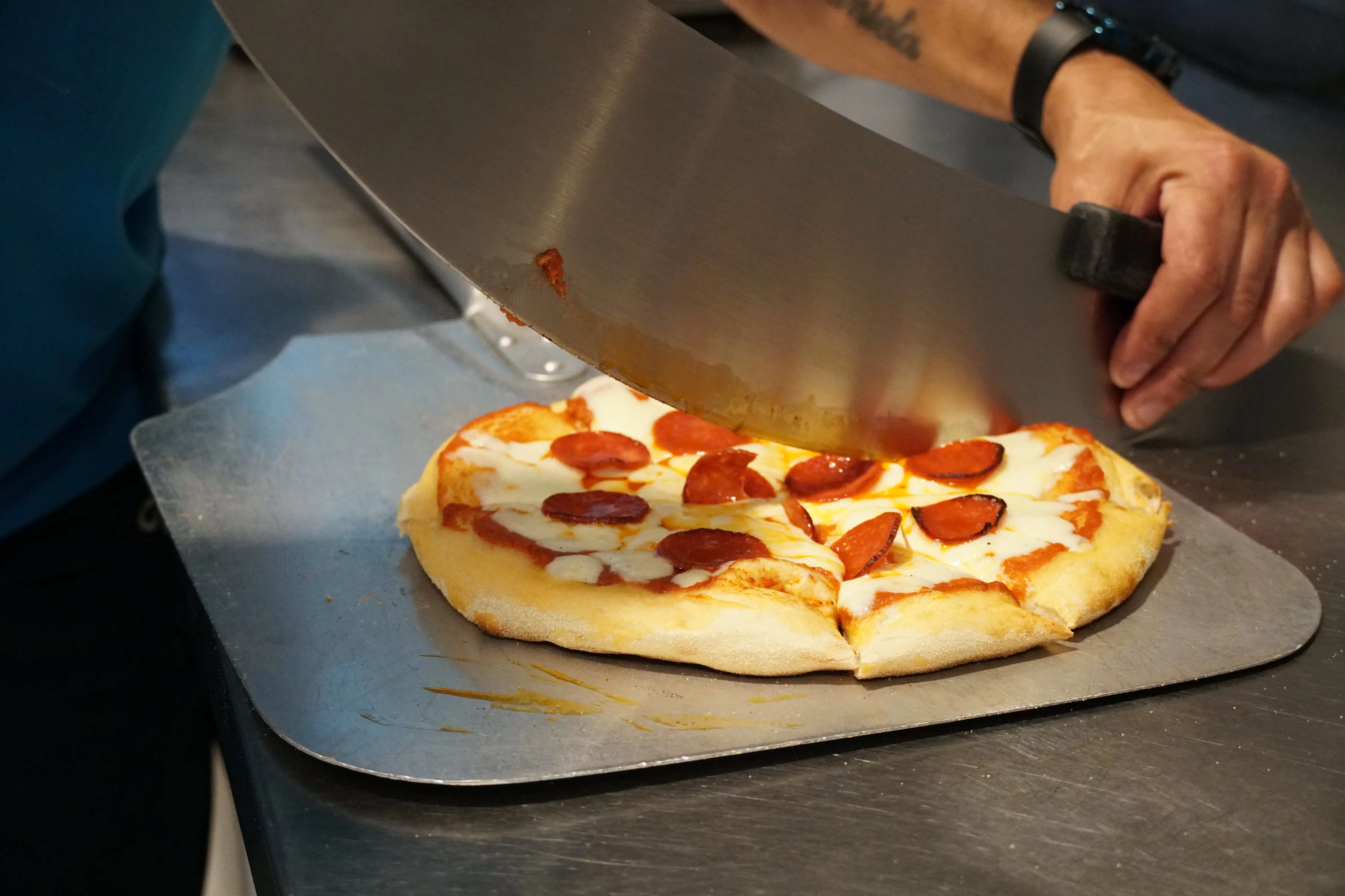 Peperoni pizza being cut by chef